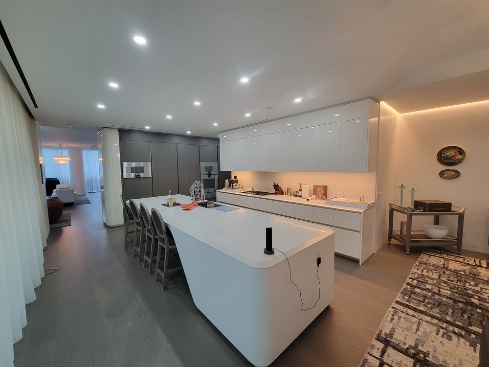 Modern open-concept kitchen with seamless integration into adjacent spaces. White high-gloss cabinetry with