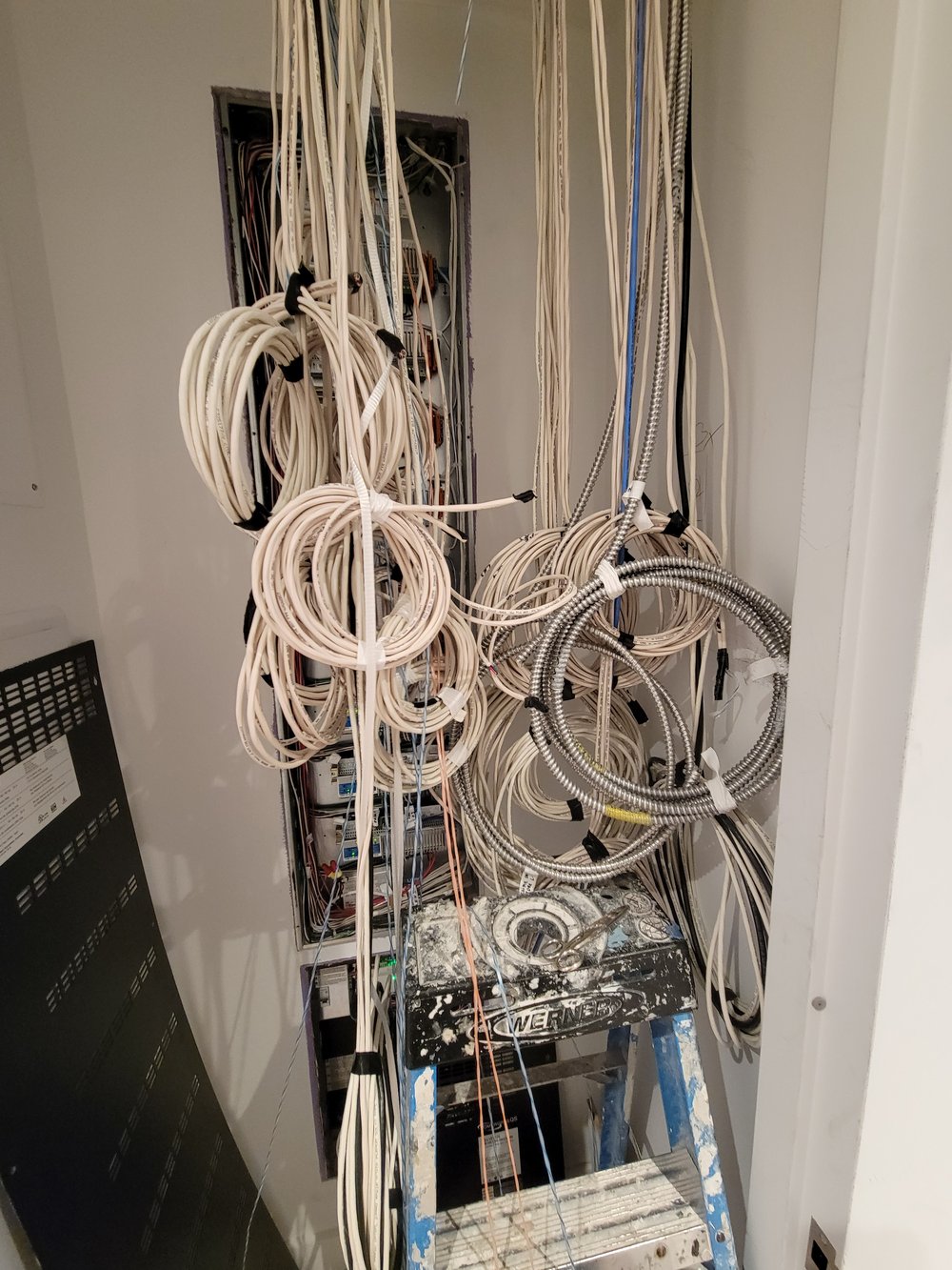 A rough-in installation photograph showing extensive AV and networking cabling work in a narrow utility