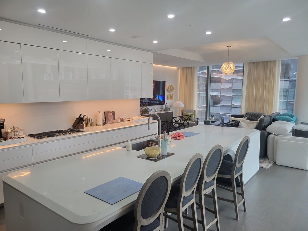Luxurious open-plan residential space combining kitchen, dining, and living areas. White lacquered cabinetry