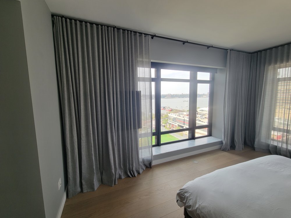 A finished luxury master bedroom showcasing a sophisticated motorized drapery installation. Floor-to-ceiling