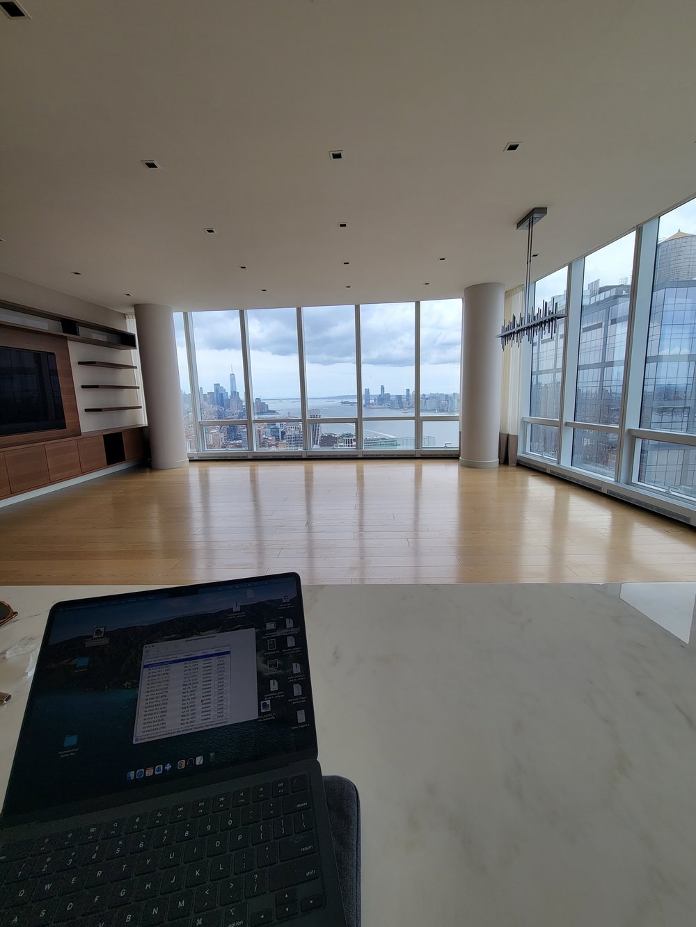 High-rise apartment interior during daytime showing extensive floor-to-ceiling windows with panoramic Hudson