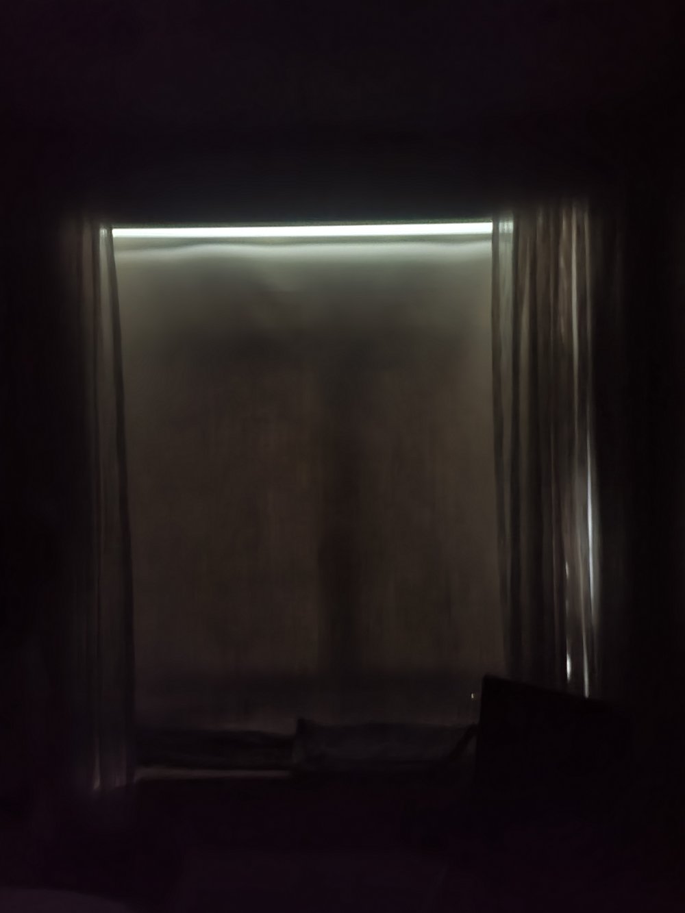 Underexposed photograph of drapery installation with accent lighting running along a horizontal track or