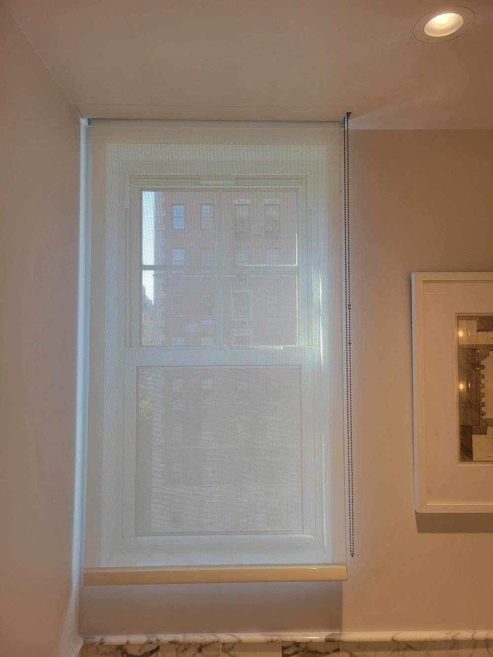 Window installation featuring motorized roman shade system with visible control cord and hardware. The