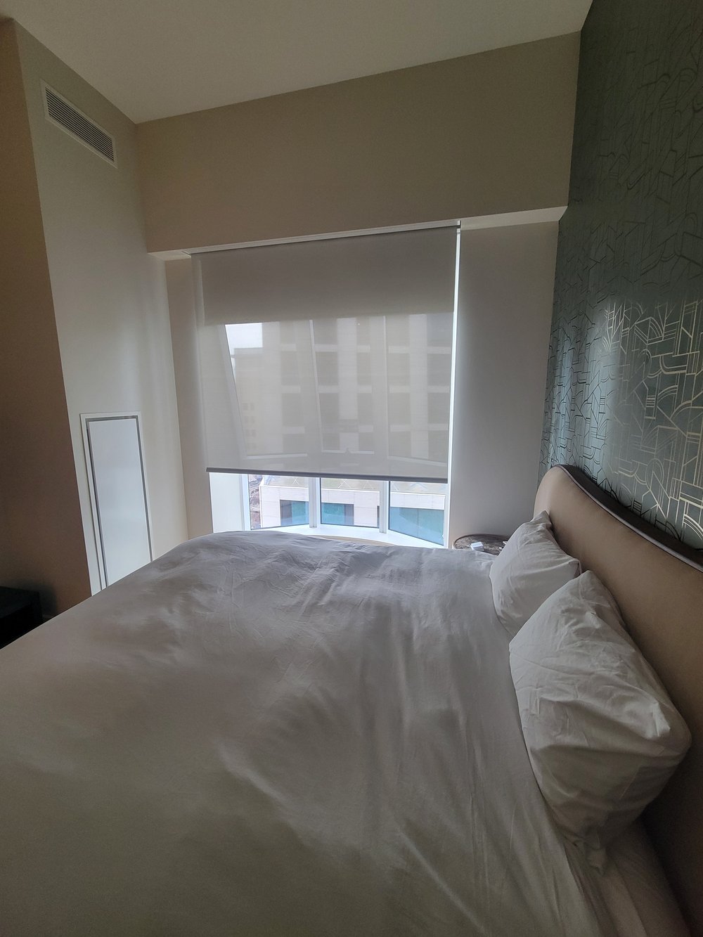 Contemporary bedroom featuring motorized roller shades with geometric patterned accent wall in muted tones.