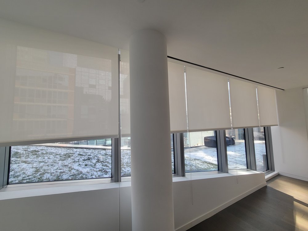 Wide-view installation of motorized roller shades across multiple large windows with Manhattan city views.