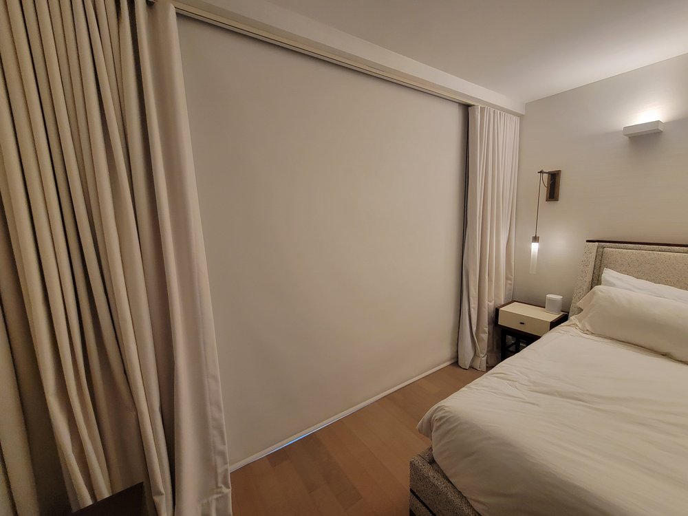 Finished bedroom with emphasis on motorized shade control and integrated lighting. A white motorized Roman