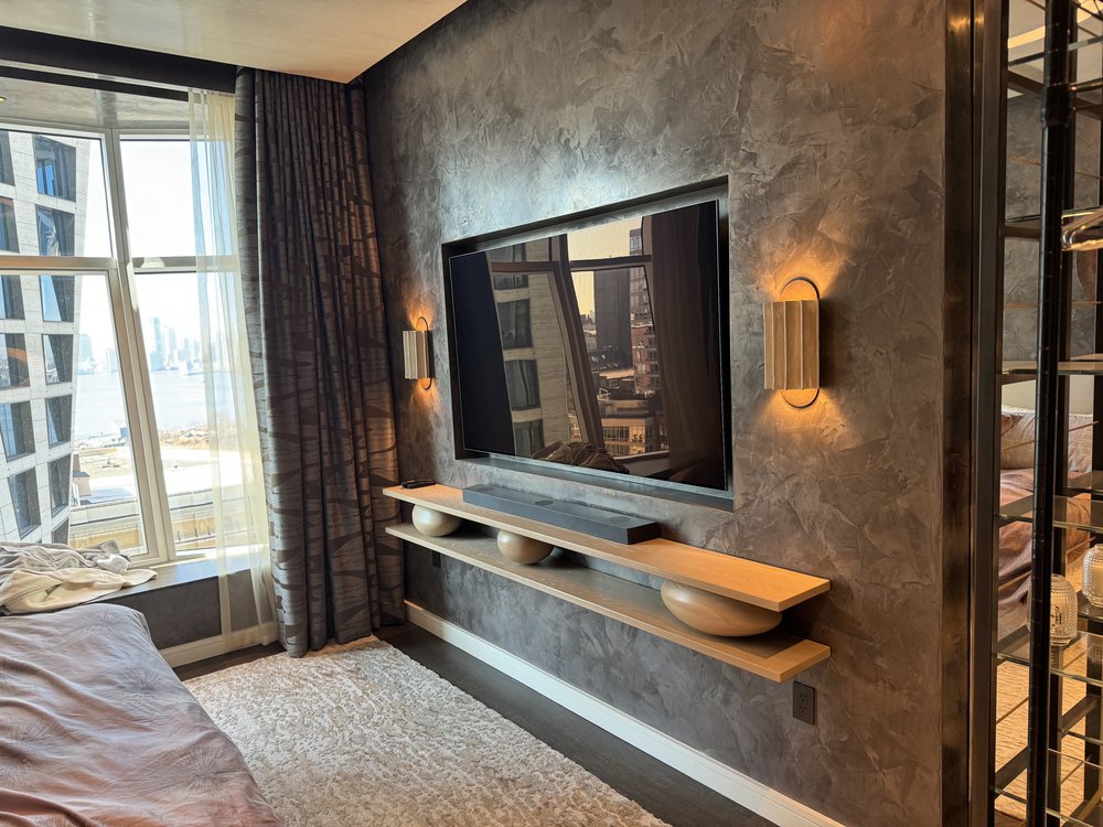 Similar view of the same master bedroom showcasing the TV installation and textured accent wall with sconce