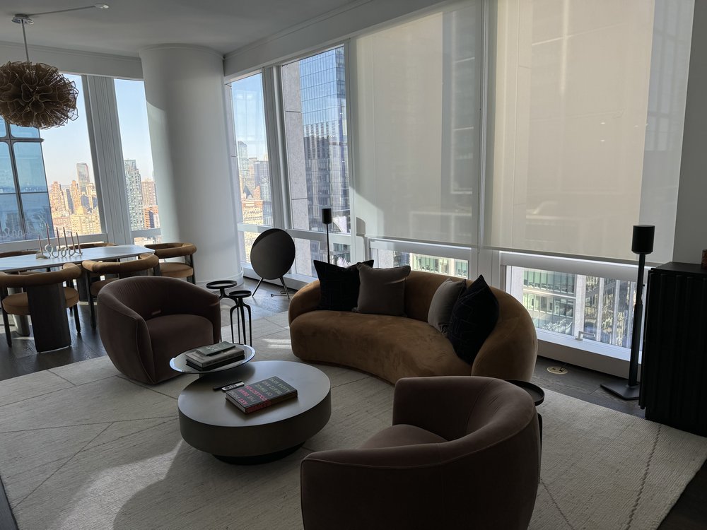 Contemporary high-rise living room with expansive windows framing a dramatic NYC skyline. The space is