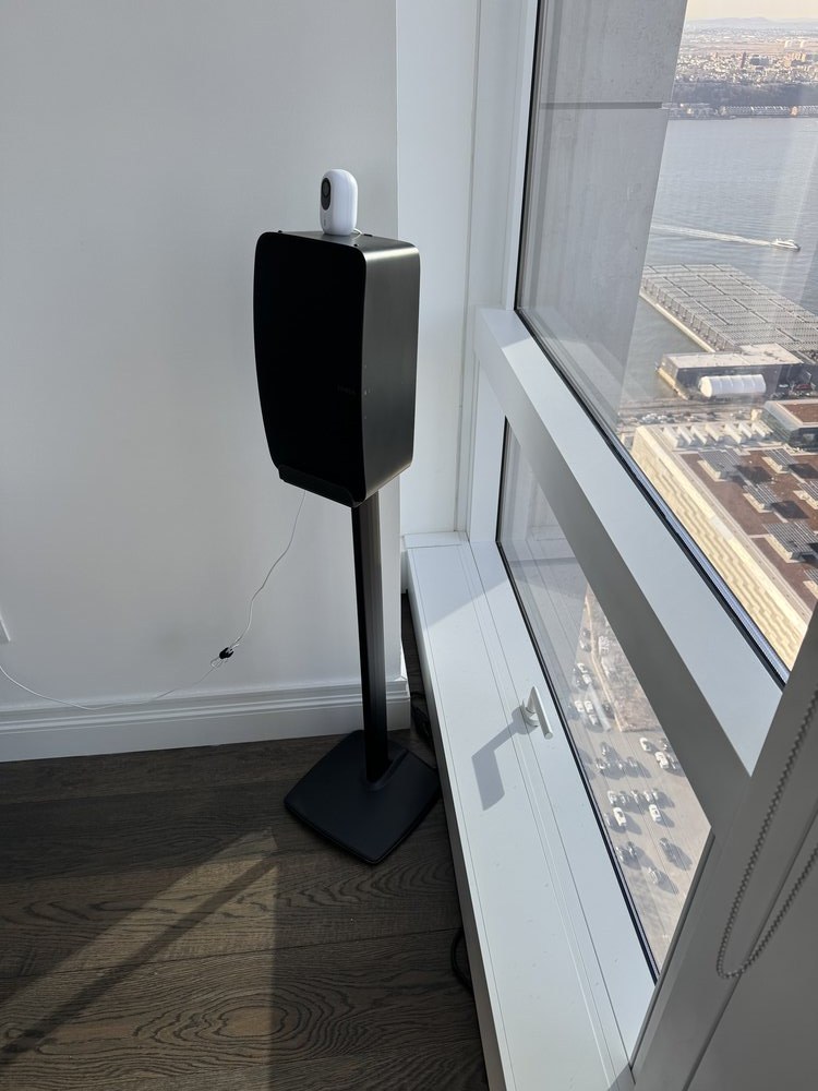 Close-up detail photograph of a motorized window shade mechanism adjacent to a dark wood-grain accent wall.
