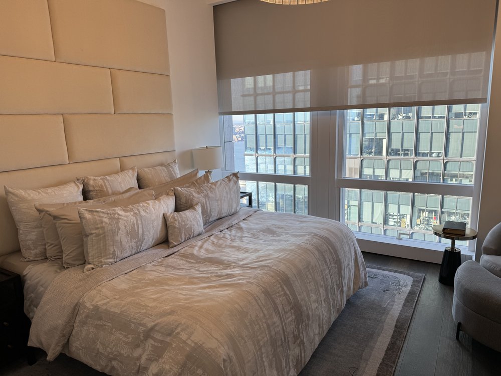 Luxurious modern bedroom with dramatic floor-to-ceiling windows showcasing NYC skyline views. The focal point