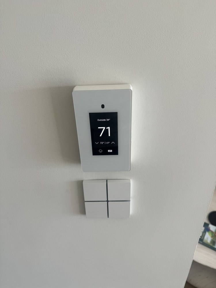 Close-up of a smart home thermostat mounted flush on drywall, displaying temperature reading of 71 degrees.