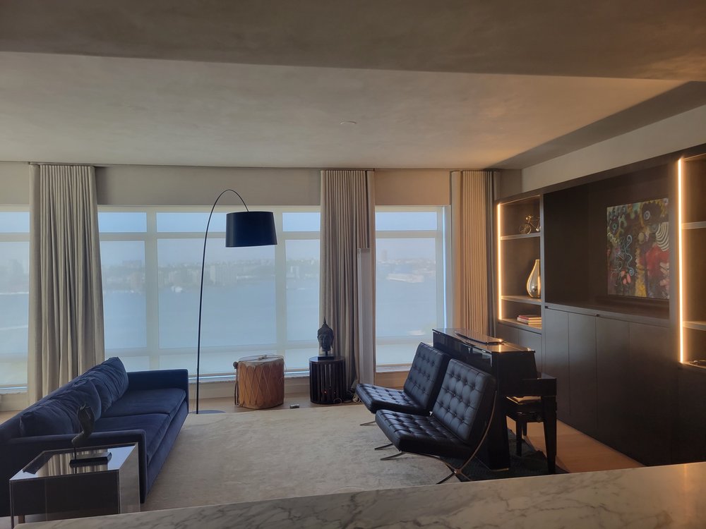 High-end contemporary living room with commanding views overlooking a waterfront cityscape. The space