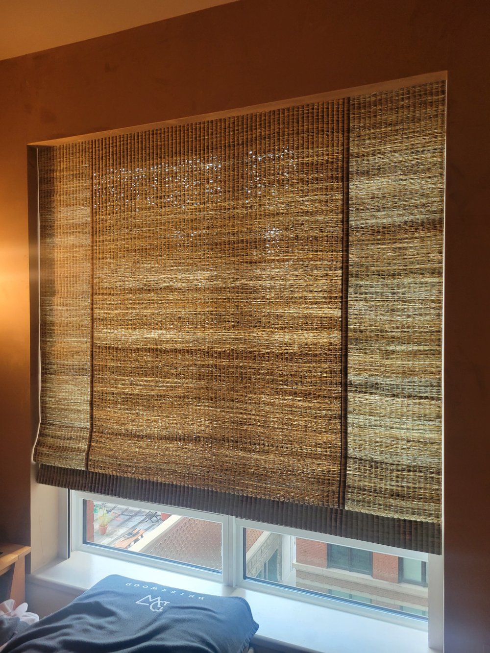 Bedroom window treatment detail showing a dual-shade system with textured woven roman shades in natural tan