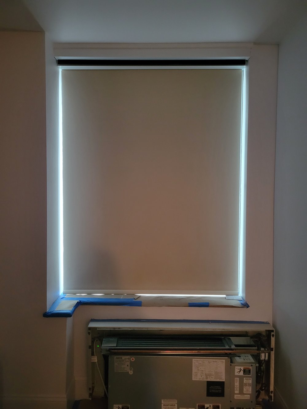 In-progress motorized roller shade installation with blue painter's tape on bottom frame corners. Identical