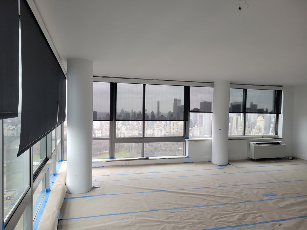 Similar window view showing motorized roller shade deployment with Manhattan cityscape including Central Park