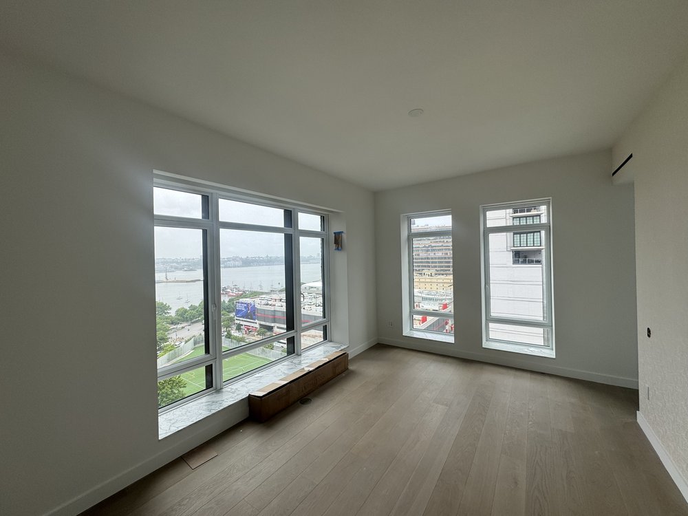 Luxury penthouse living room with floor-to-ceiling windows overlooking Manhattan's waterfront and skyline.