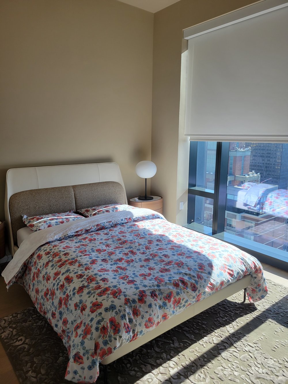 A finished high-rise bedroom photographed in natural light showcasing a modern aesthetic. The room features a