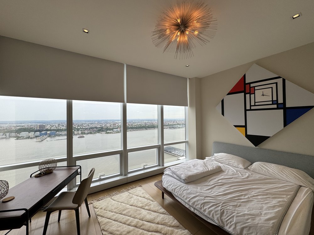 Modern high-rise bedroom with sophisticated minimalist aesthetic. Floor-to-ceiling windows frame expansive