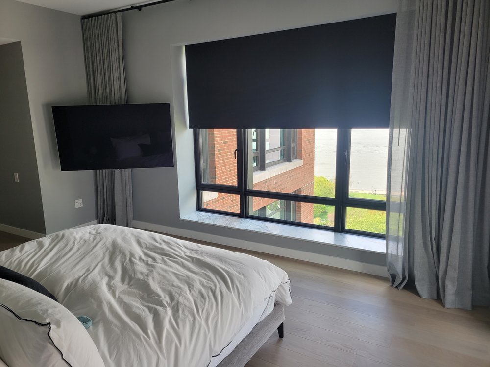 A finished luxury master bedroom featuring integrated entertainment and light-control systems. The room
