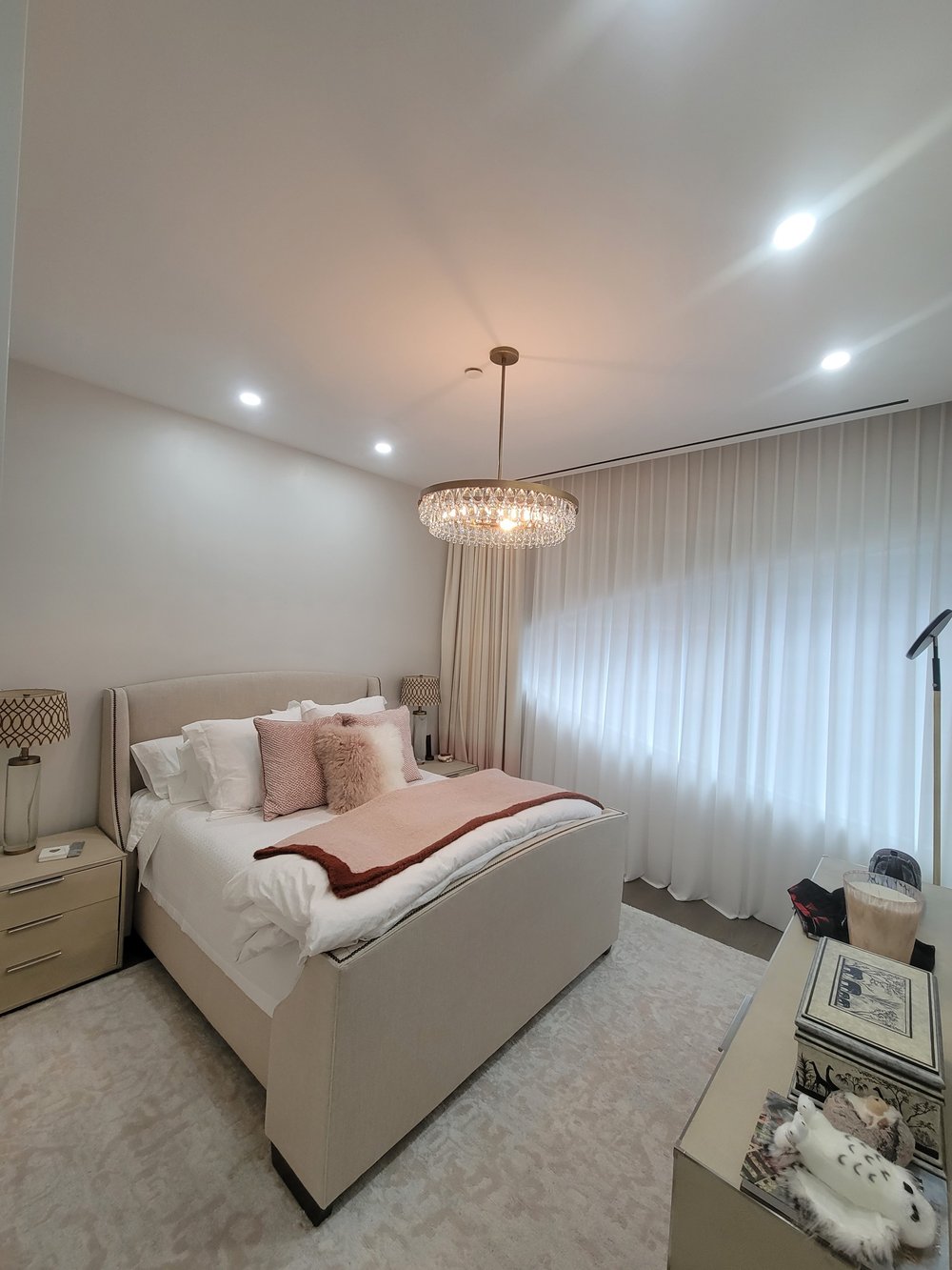 Elegantly appointed master bedroom with sophisticated lighting and window treatments. Large white upholstered