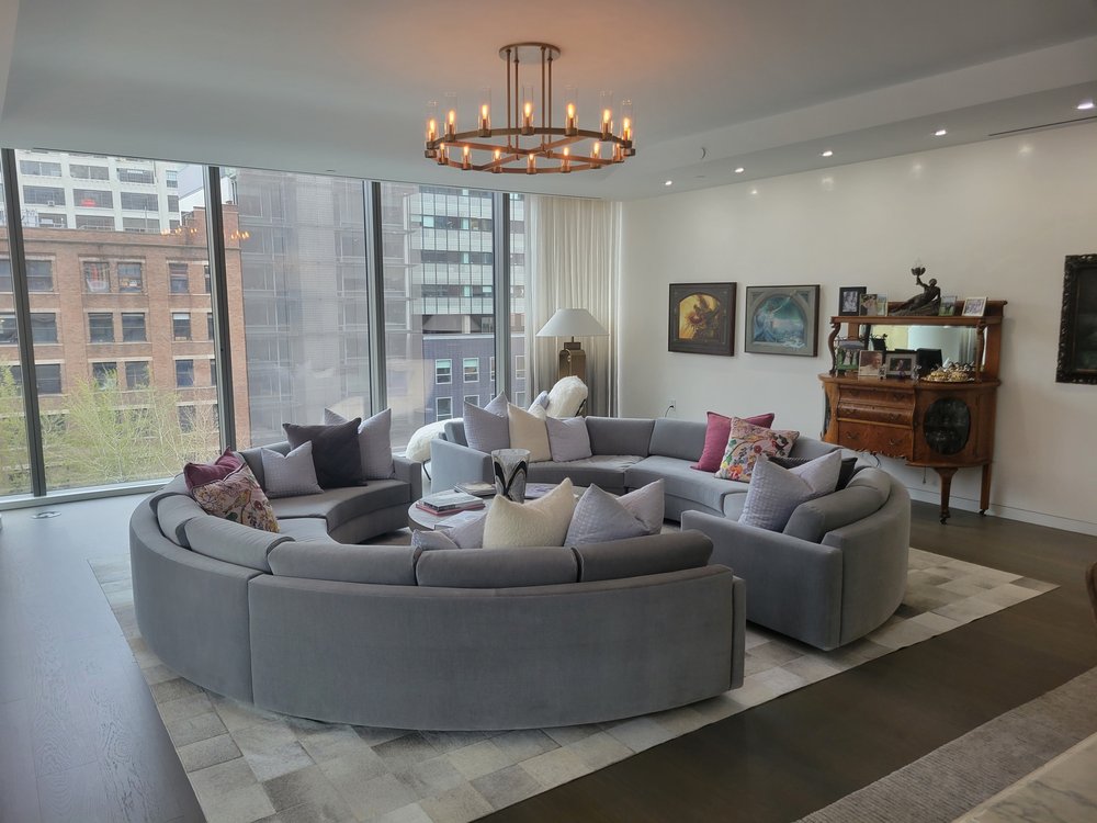 Duplicate angle of the same expansive living room with curved gray sectional, chandelier overhead,