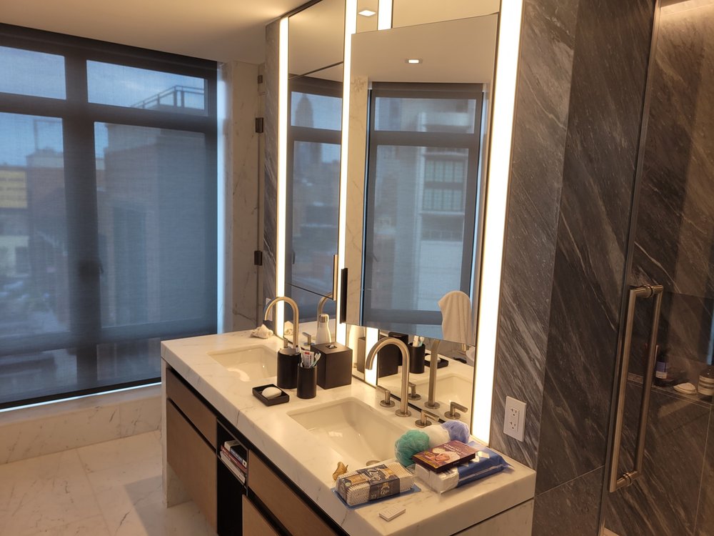 Luxury bathroom with marble-clad accent wall in gray and white tones. Large lighted mirror with integrated
