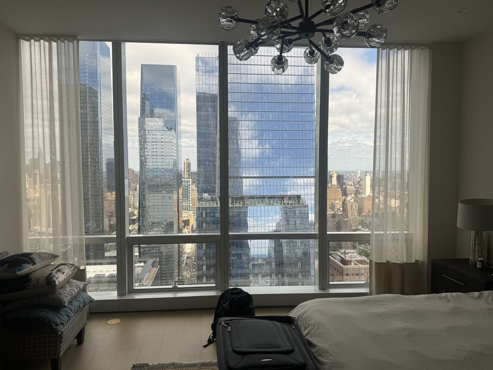 Luxurious high-rise master bedroom with spectacular floor-to-ceiling windows framing iconic Manhattan skyline
