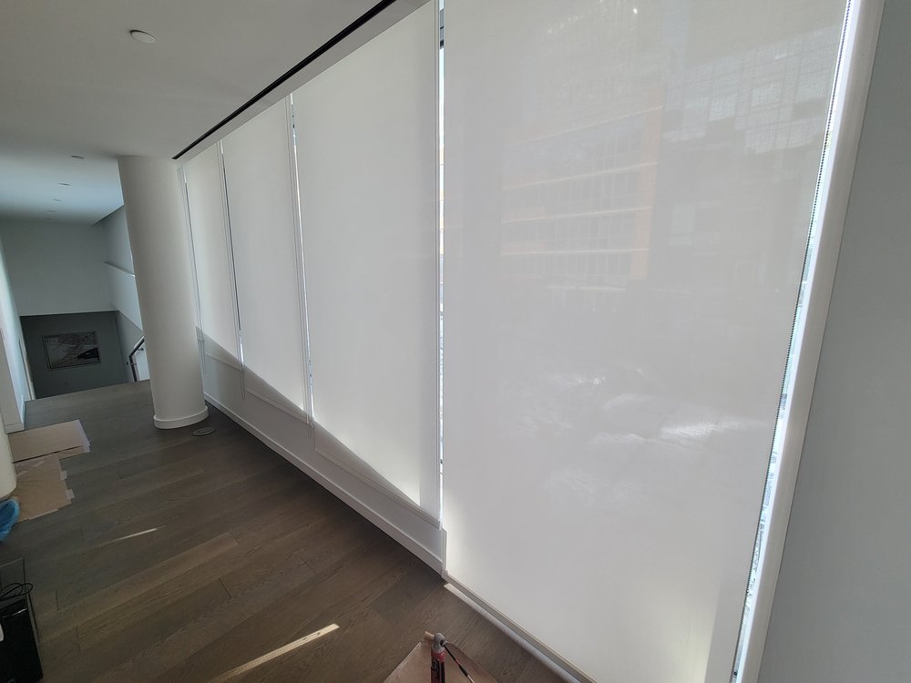 Modern motorized roller shades installed on large windows with Manhattan cityscape views visible beyond. The