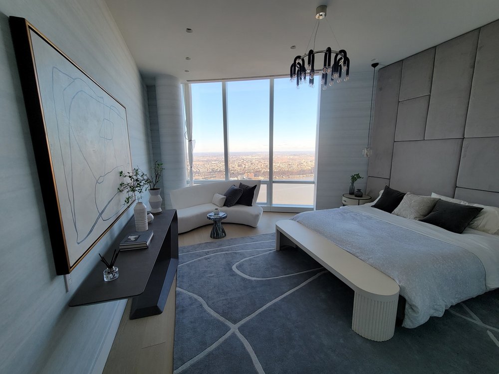 A contemporary high-rise bedroom interior with minimalist design featuring an upholstered headboard panel in