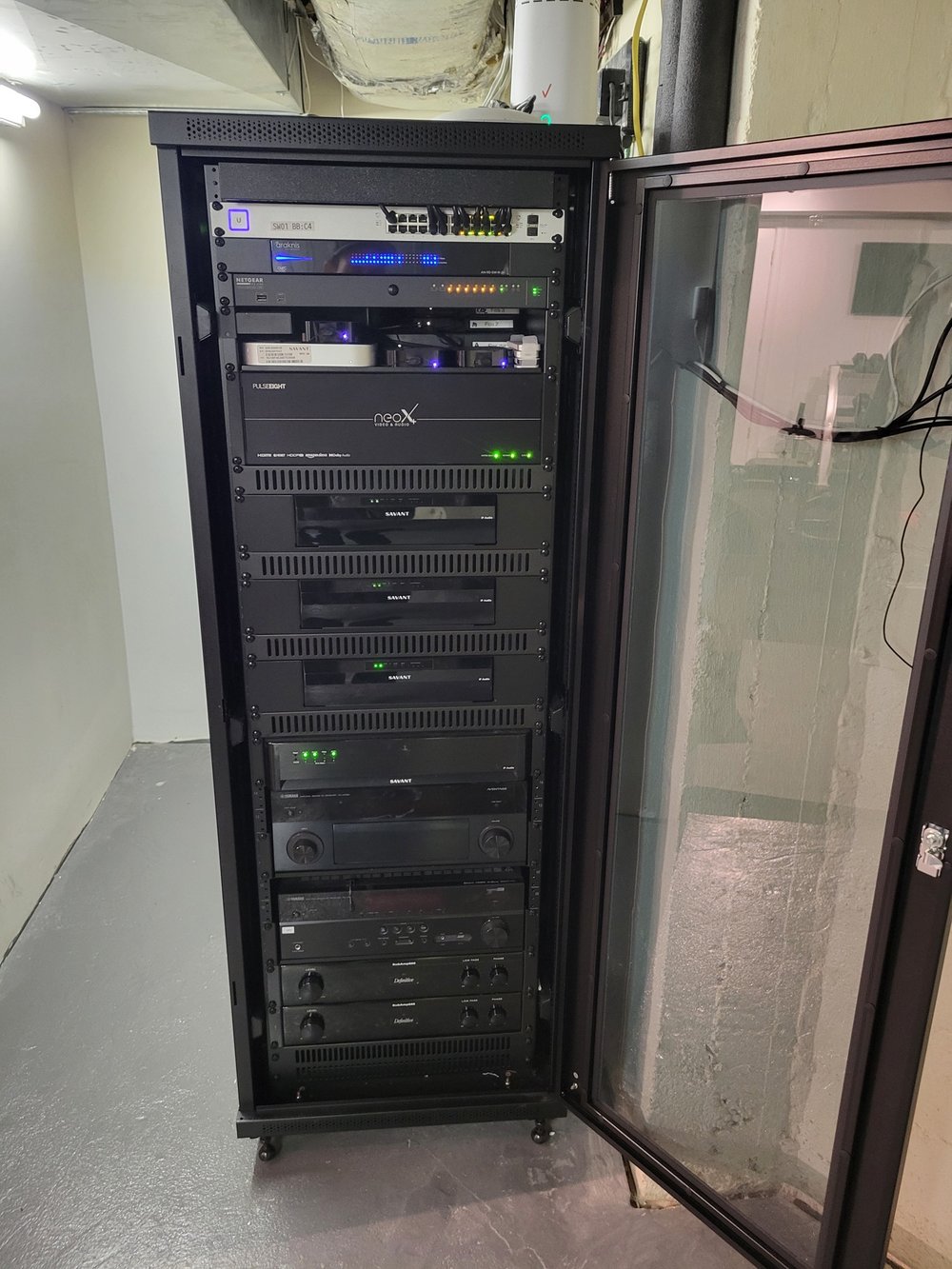 A fully installed AV equipment rack mounted in a utility space, featuring multiple black units with