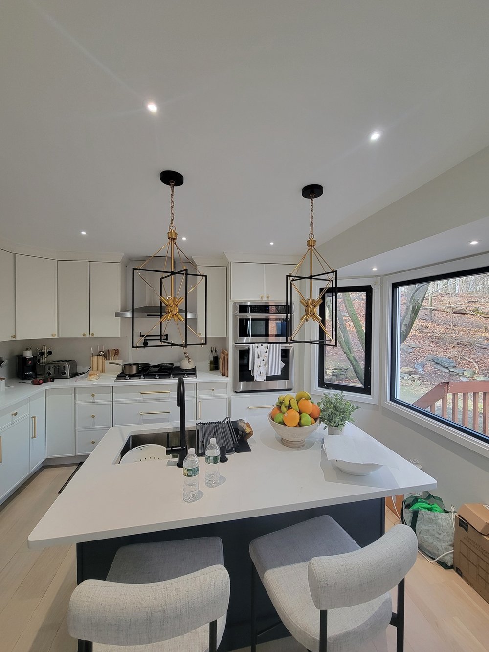 Modern kitchen with white cabinetry, black island counter, brass and black geometric pendant lights.