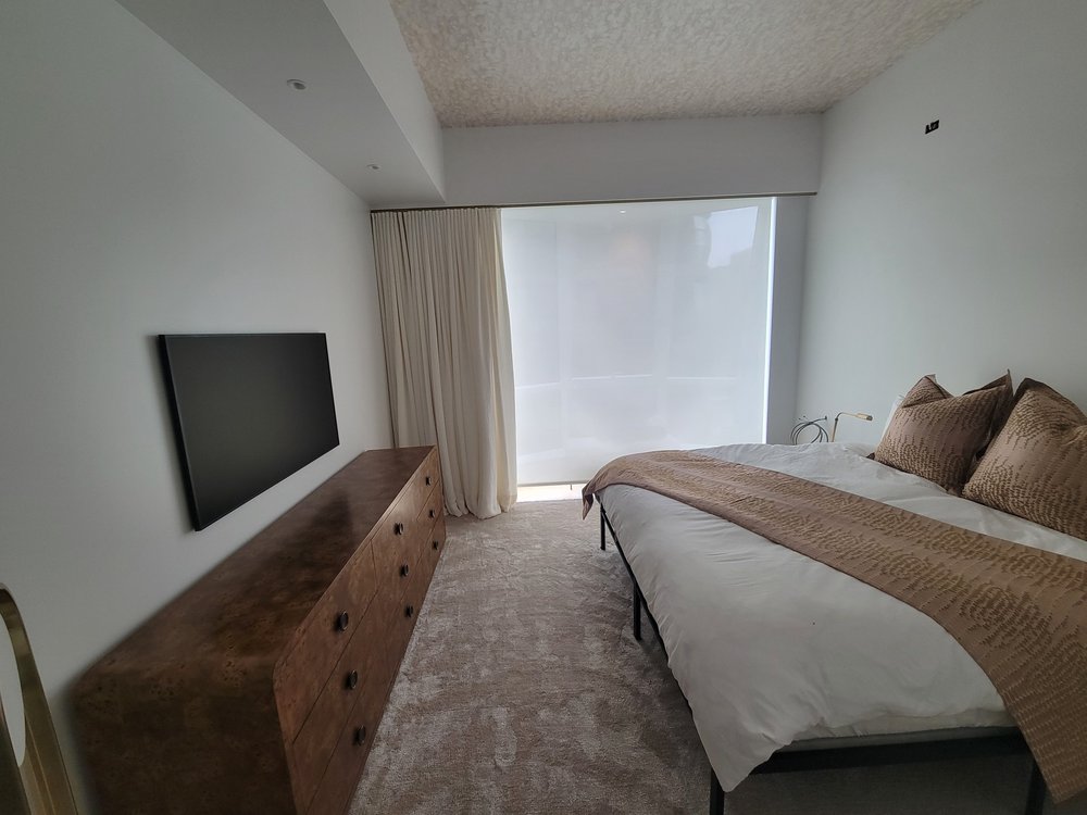 Master bedroom showcasing wall-mounted flat-screen TV, wooden dresser with dark stain, multiple recessed