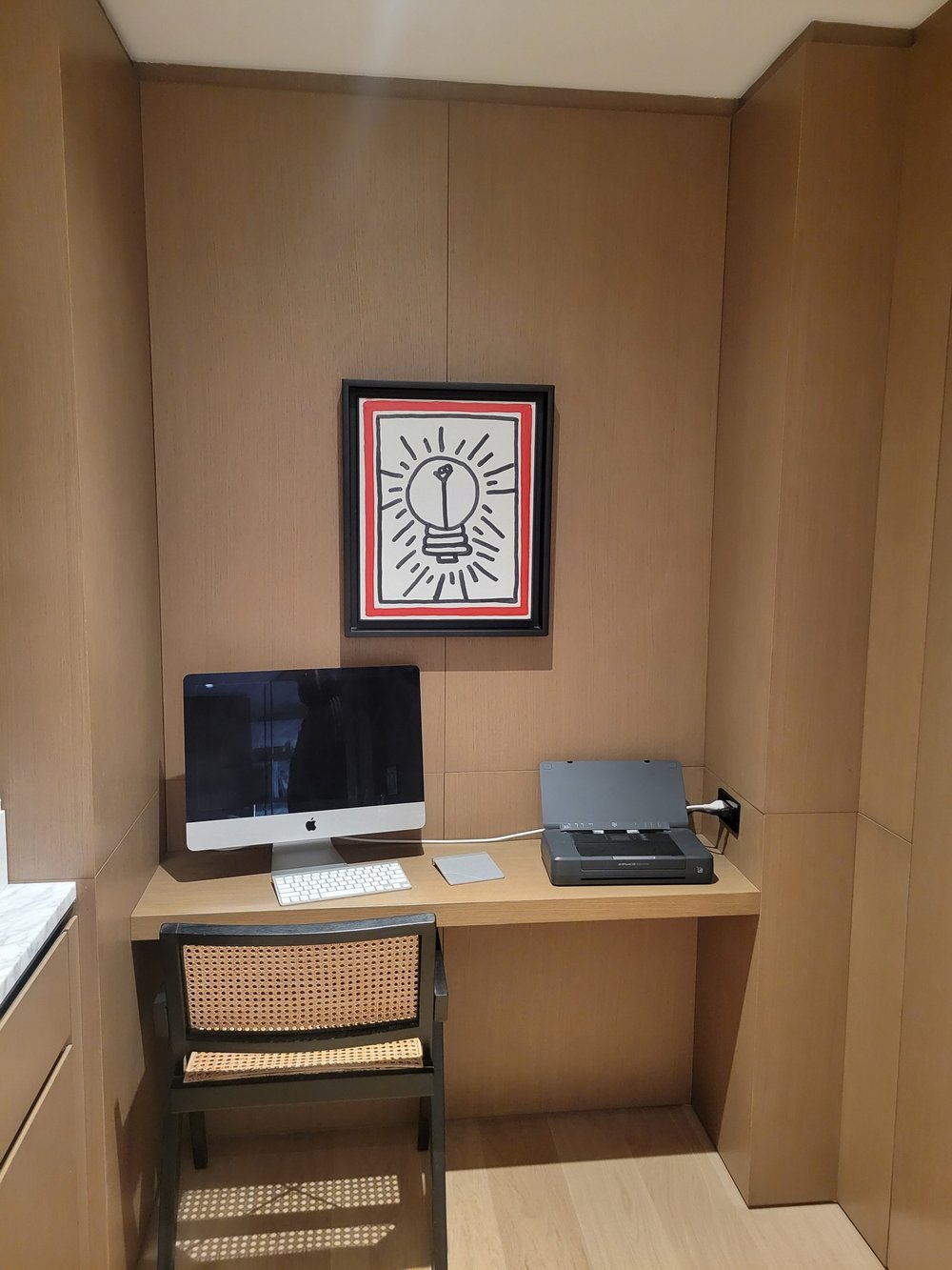 Finished closet office with light wood cabinetry and soft beige walls. Desktop features an Apple iMac with