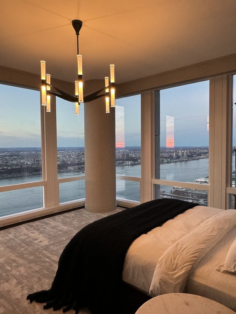 Bedroom photographed from an elevated angle, featuring a bed with cream and black layered linens, large