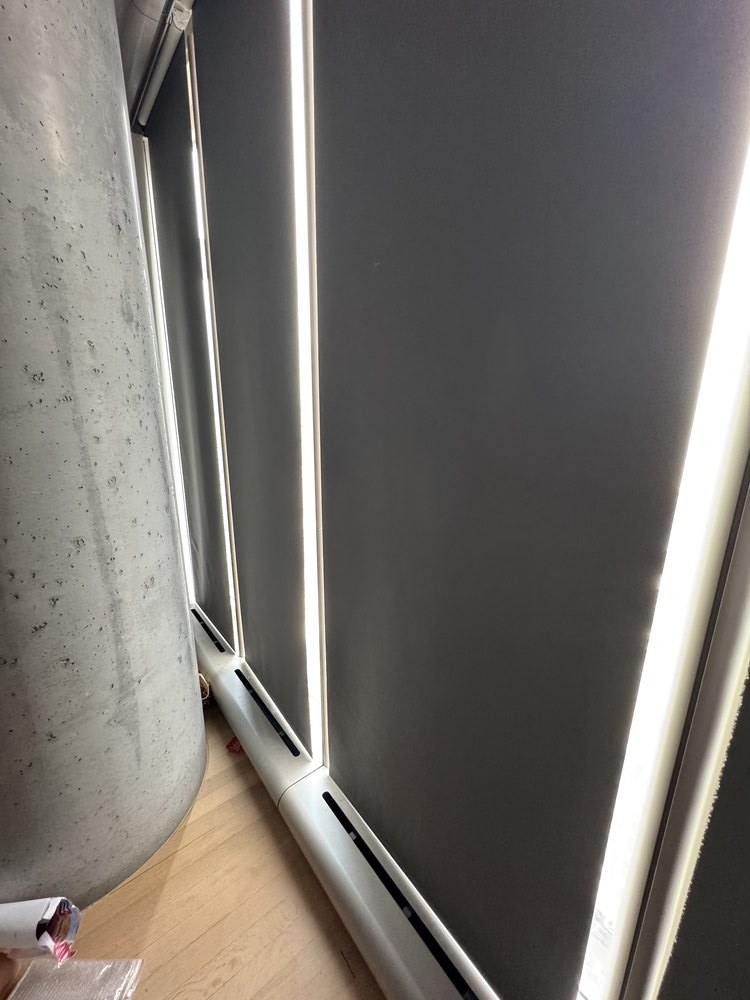 Installation progress photo showing motorized roller shade hardware being mounted in a ceiling cavity. The