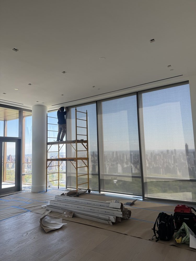 Large open living space in active renovation with expansive windows overlooking the city skyline. A motorized