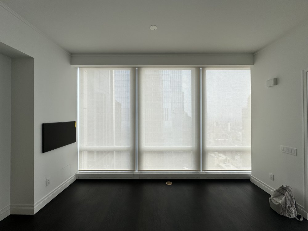 Clean minimalist living room with white walls and dark hardwood flooring. Flat-screen TV mounted on left