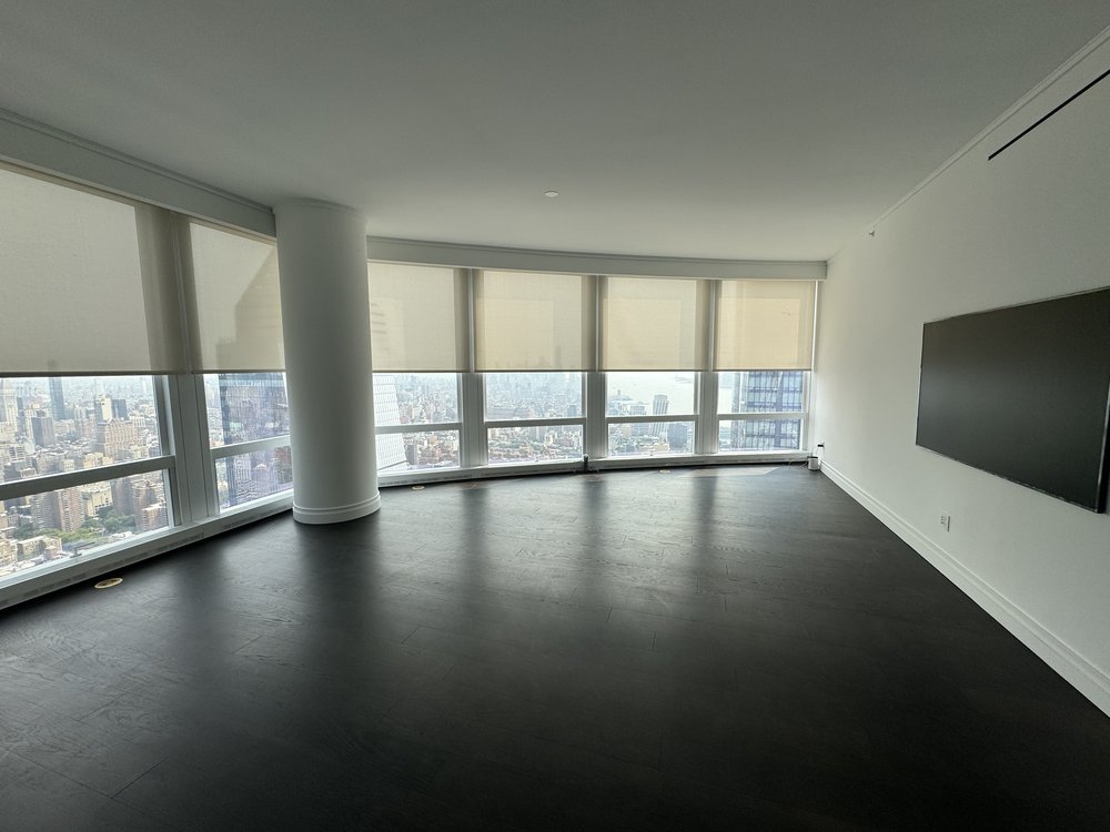 High-rise corner living room with expansive curved window wall offering dramatic urban skyline views. White