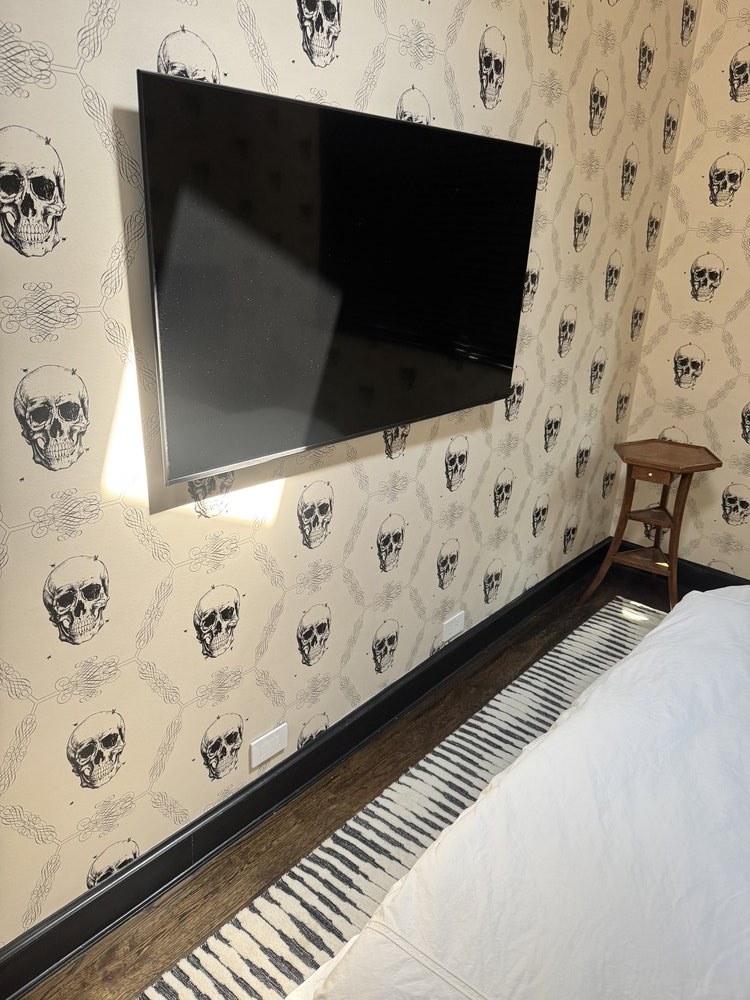 Bedroom interior with mounted black flat-screen TV on patterned wallpapered ceiling featuring decorative