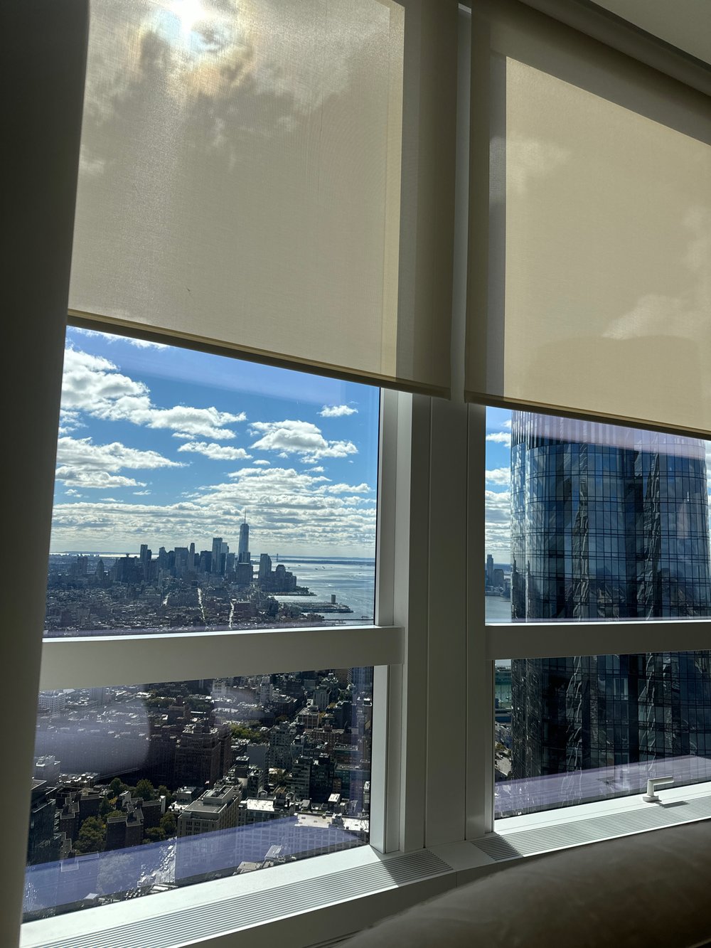 High-rise residential interior photographed through large windows with motorized roller shades partially